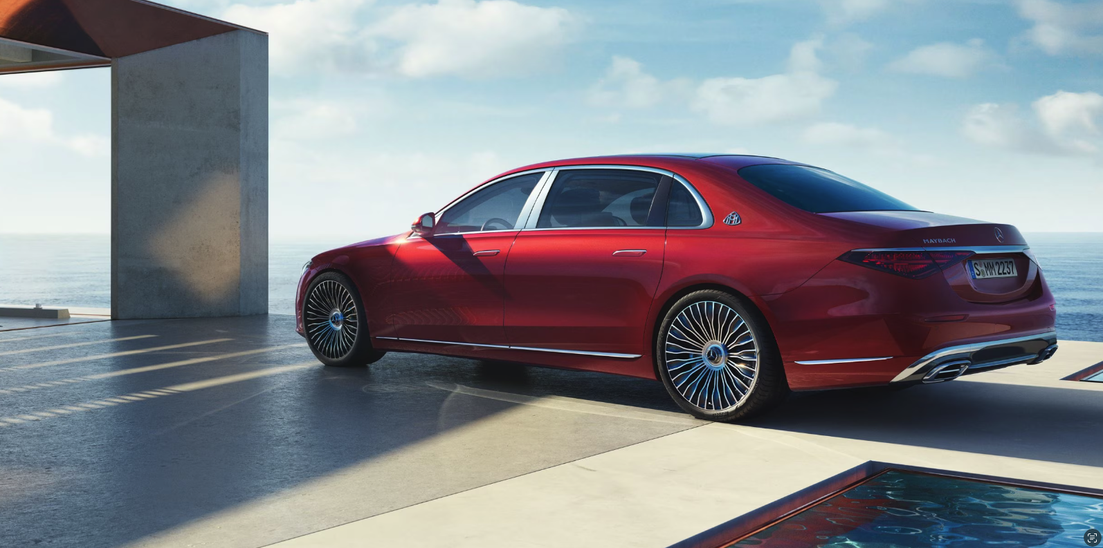Metallic red Mercedes-Maybach S-Class luxury sedan parked on modern white terrace overlooking ocean at sunset, rear three-quarter view showcasing elegant proportions and chrome details